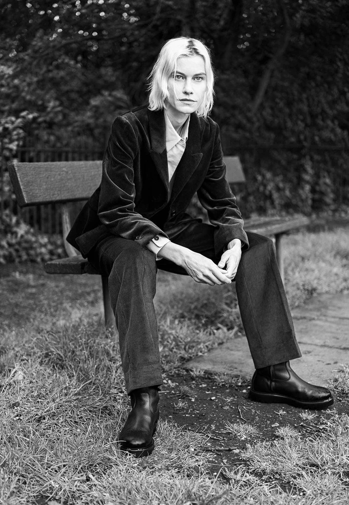 Model wearing a dark velvet blazer and trousers seated on a park bench outdoors