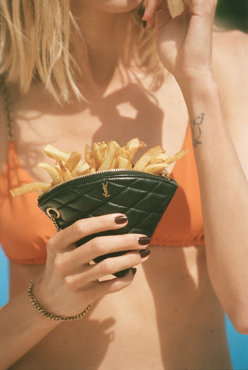 Model holding a black quilted leather pouch filled with French fries, wearing an orange bikini top