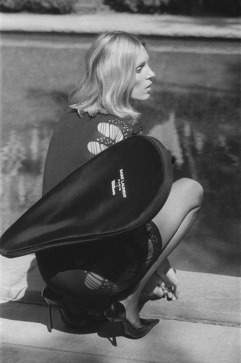 Model Anja Rubik crouches by a pool holding a Saint Laurent tennis racket case for the Summer 2024 campaign