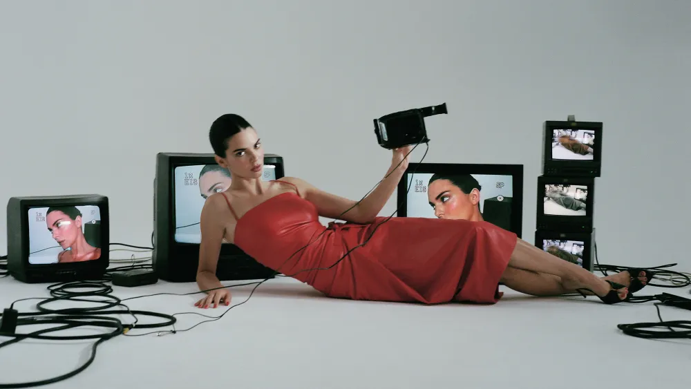 Model Kendall Jenner reclining in a red leather dress among vintage CRT television monitors for FWRD Fall 2024 campaign
