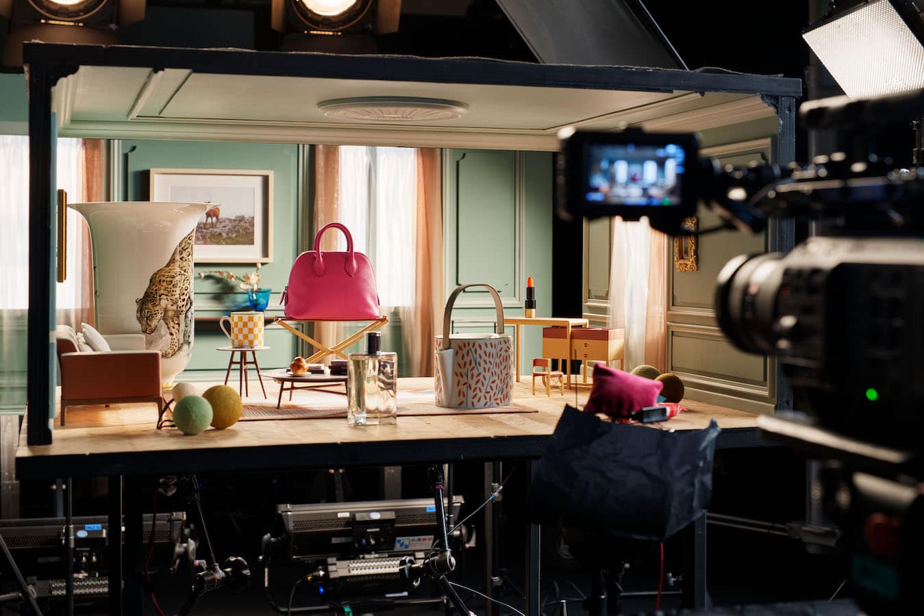 Behind-the-scenes view of a miniature set featuring a pink leather handbag and props filmed with a professional camera.