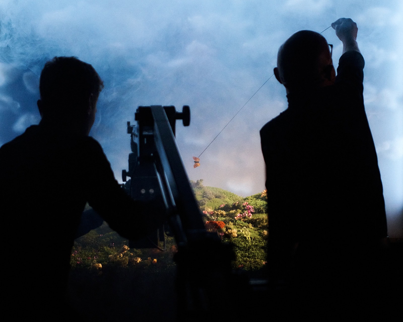 Silhouetted figures operating a camera crane in front of a miniature landscape backdrop