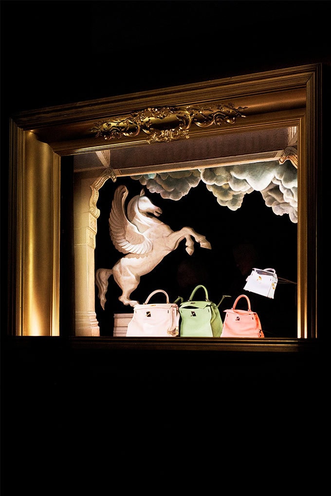 Pegasus sculpture and luxury leather handbags inside an ornate gilded picture frame against a dark background.