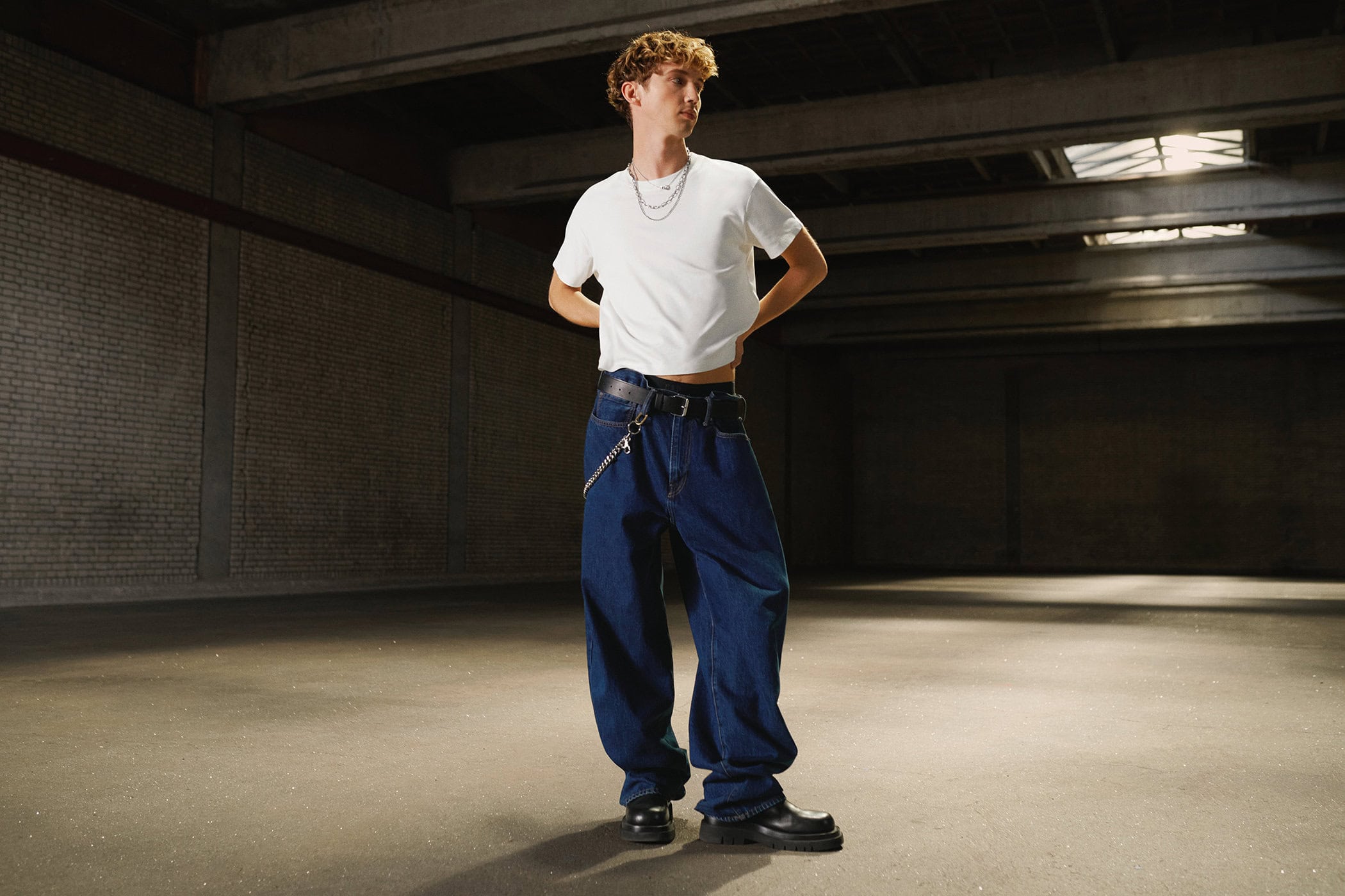 Troye Sivan standing in a large warehouse wearing a white t-shirt and baggy blue jeans for Gap Get Loose campaign