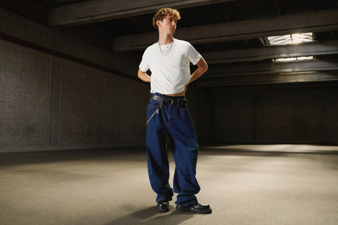 Troye Sivan standing in a large warehouse wearing a white t-shirt and baggy blue jeans for Gap Get Loose campaign