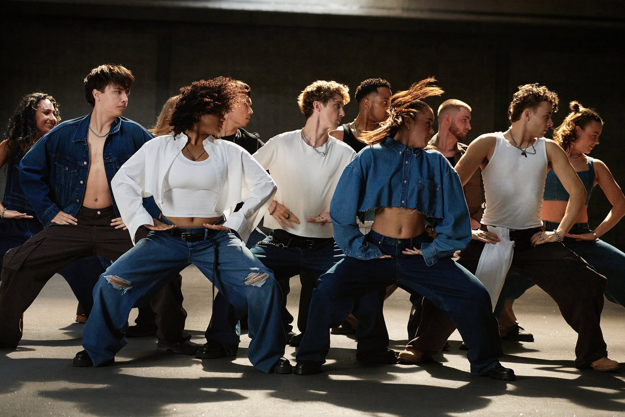 Group of dancers in denim and white t-shirts posing in a low-lit industrial space for the Gap Get Loose campaign.