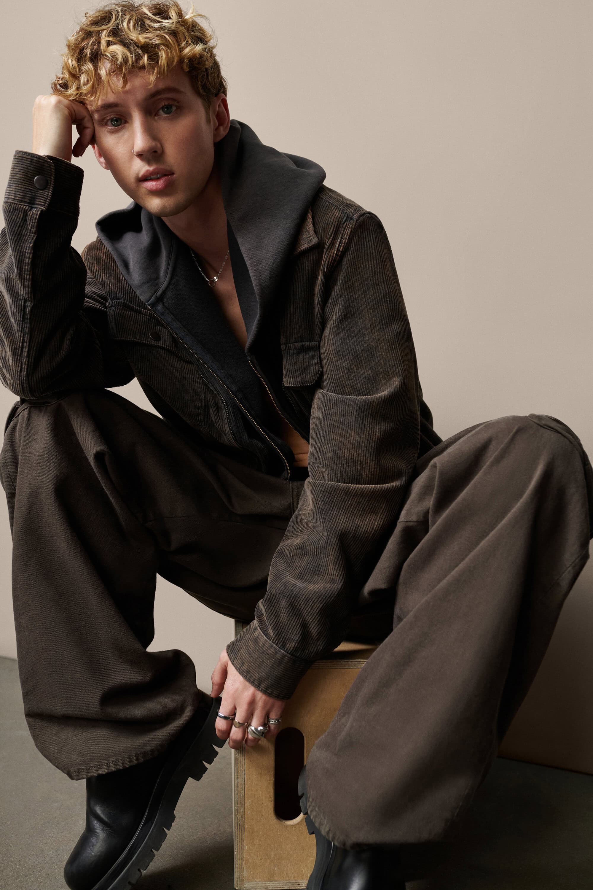 Troye Sivan posing in a brown corduroy jacket and wide-leg trousers against a neutral studio backdrop for Gap.