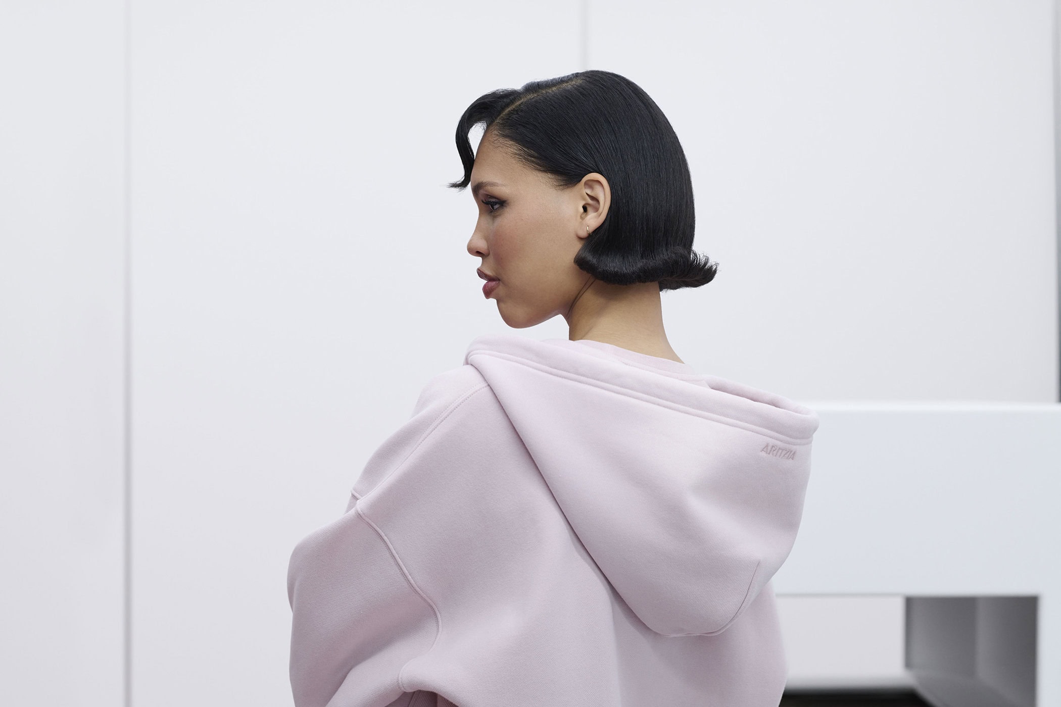 Model Nara Aziza Smith in a pink hoodie with styled black bob hair against a white background for Aritzia