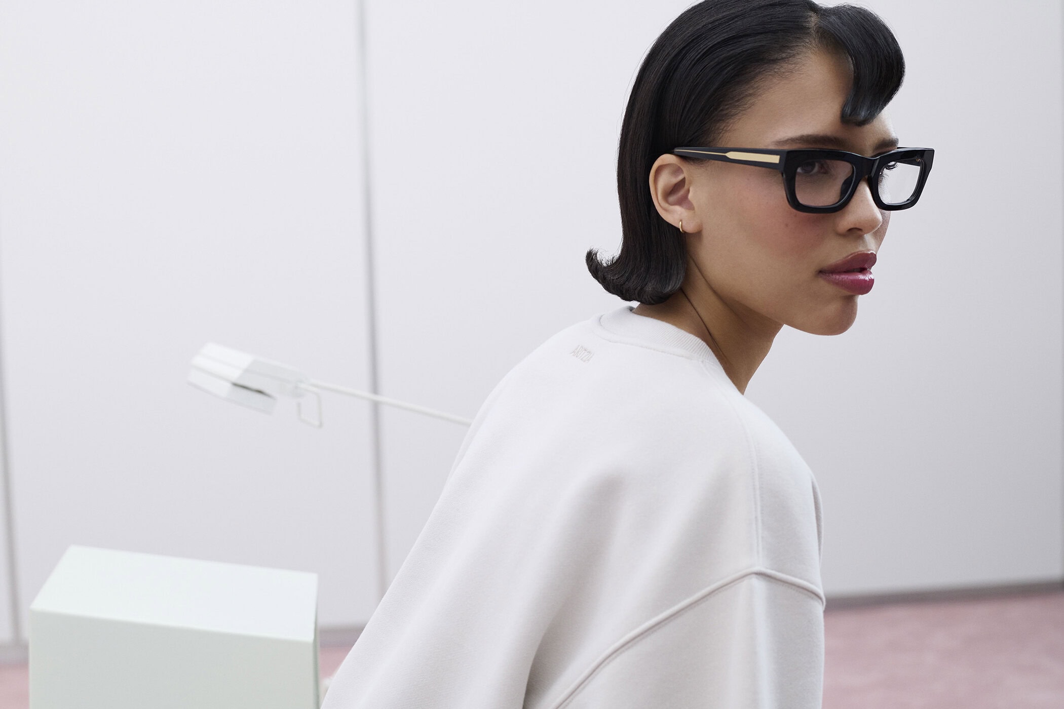 Model Nara Aziza Smith wearing thick black glasses and a white sweatshirt in the Aritzia Sweatfleece 2024 ad campaign.
