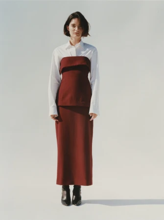 Woman with short dark hair wearing a white shirt and burgundy tube top with matching long skirt against a plain white background