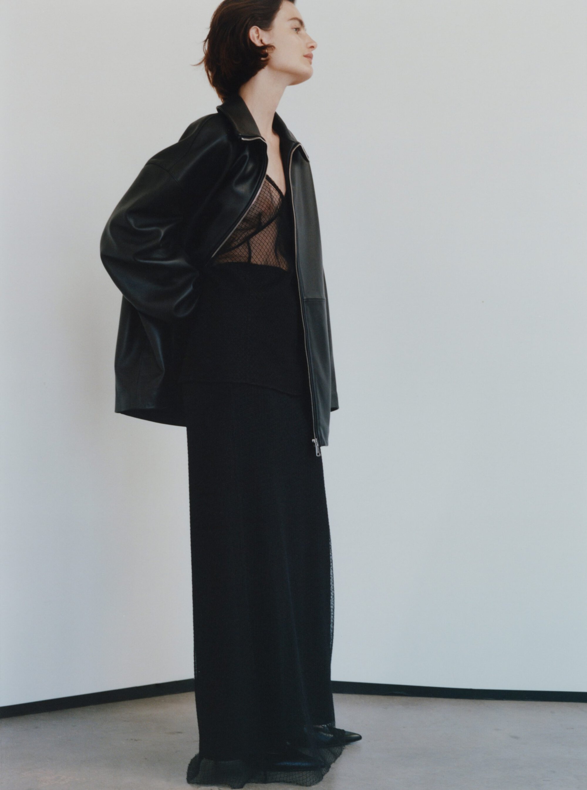 Model in black leather jacket and long black skirt against a white studio background
