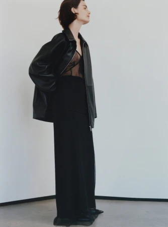 Model in black leather jacket and long black skirt against a white studio background