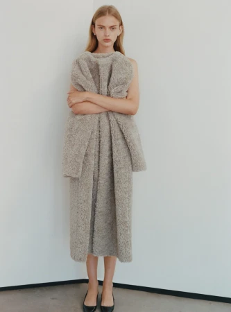 Model standing against a plain white background wearing a textured grey coat with crossed arms