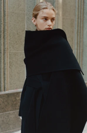 Model in a black structured coat standing against a stone building exterior for Rue Sophie Fall 2024 campaign