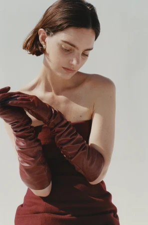 Model wearing burgundy leather opera gloves and a matching dress against a plain white studio background.