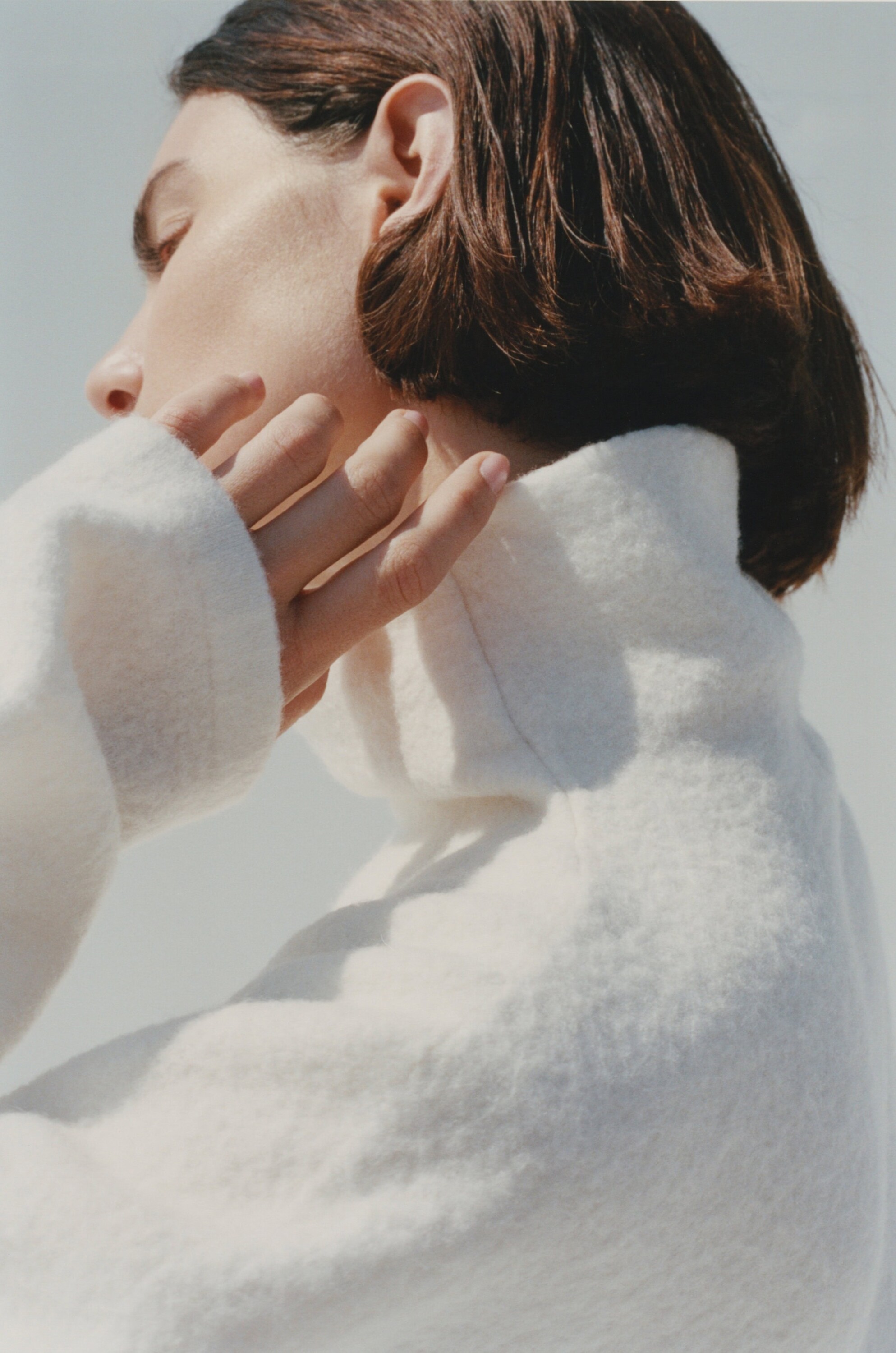 Close-up portrait of a woman wearing a white turtleneck sweater against a pale background