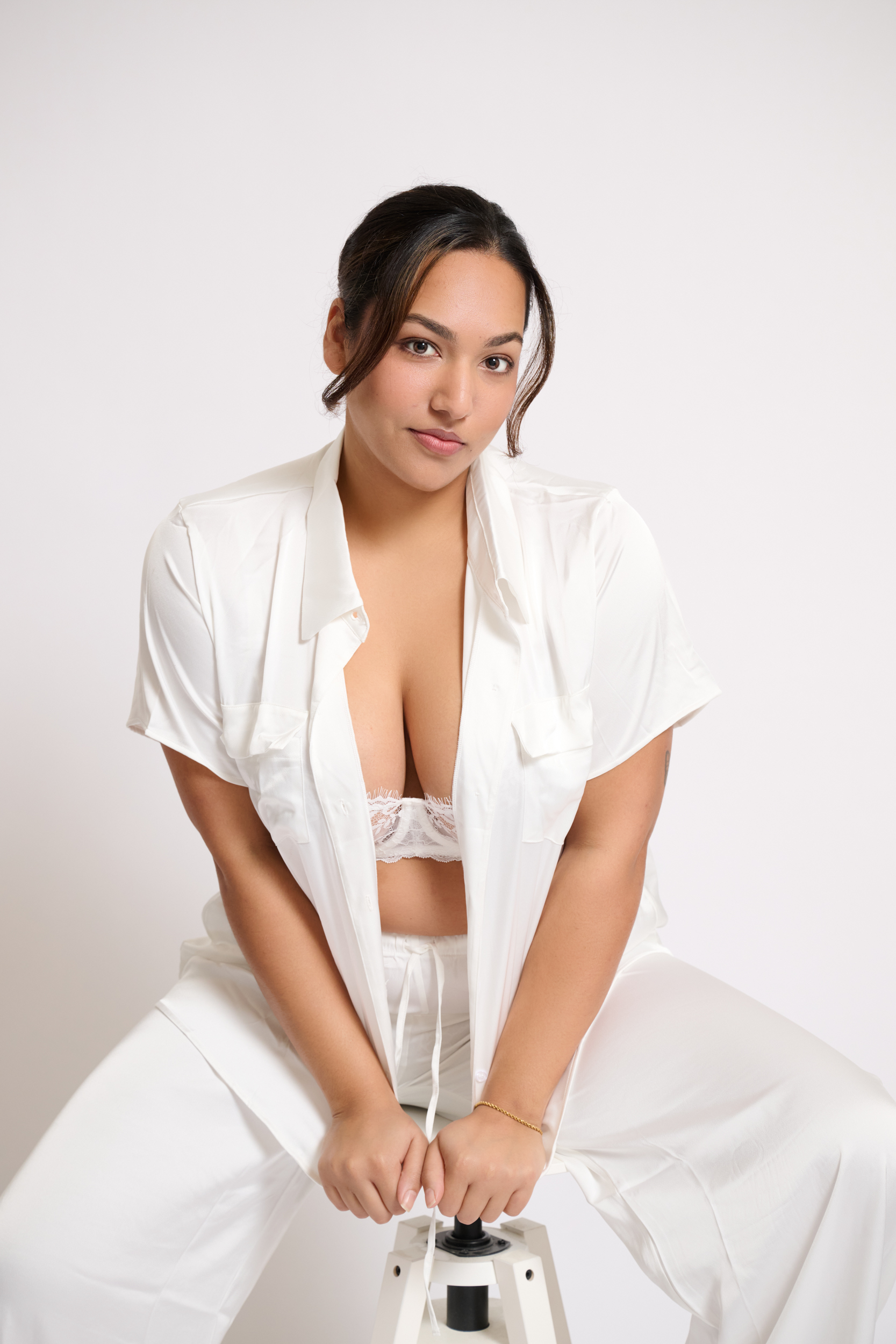 Model Shrayaarya wearing white shirt and trousers sitting on a stool against a white seamless background