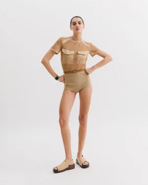 Full-length portrait of a female model wearing a tan mesh top and shorts against a seamless white background.