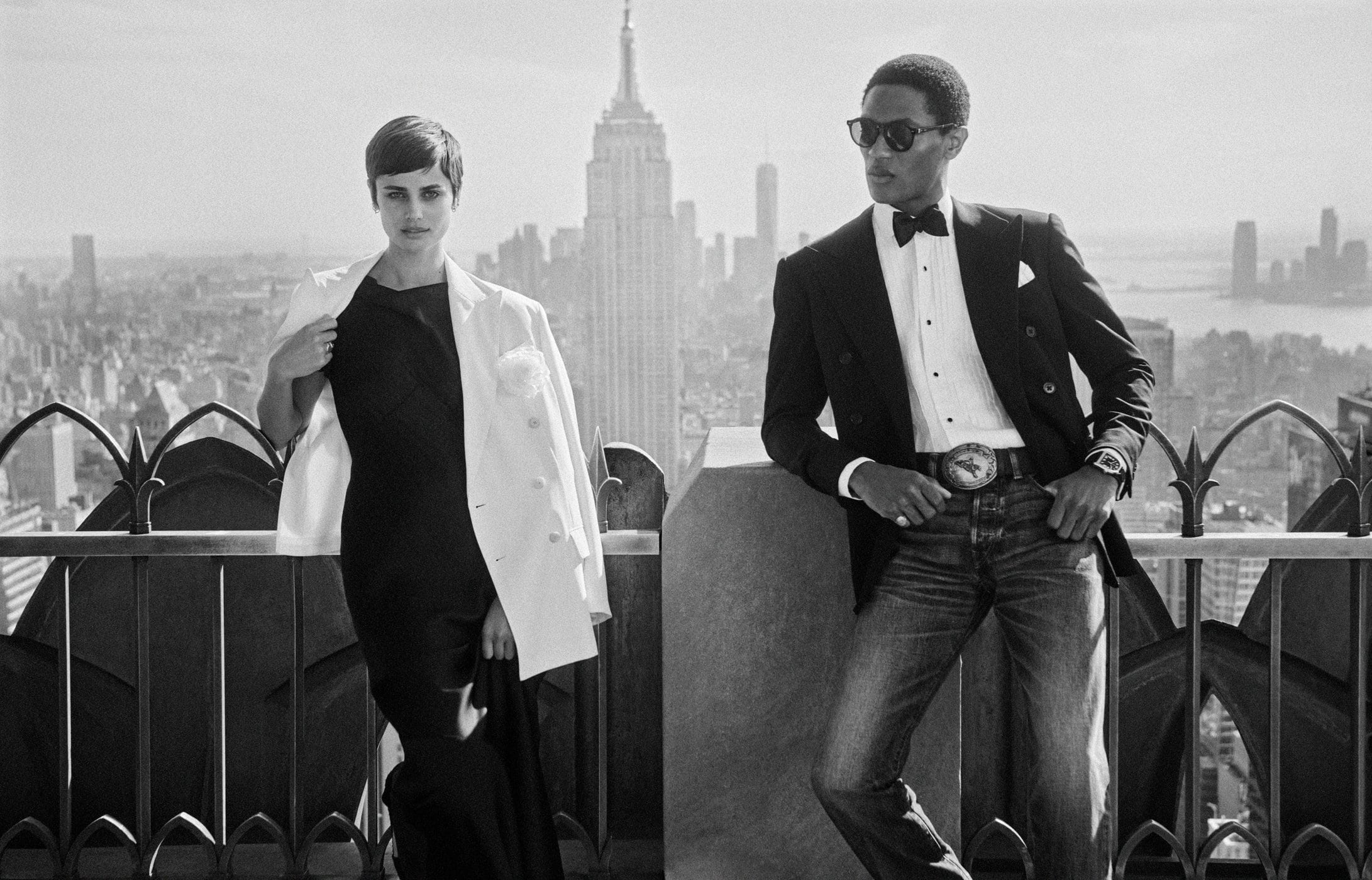 Black and white portrait of a man and woman posing on a New York rooftop with the skyline behind them.