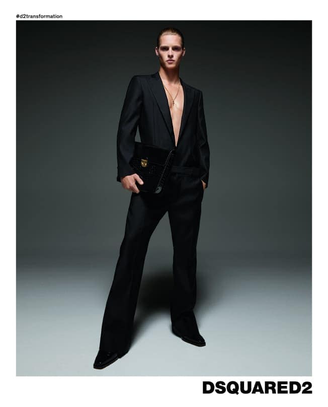 Male model in a black suit holding a dark handbag against a grey seamless background for Dsquared2