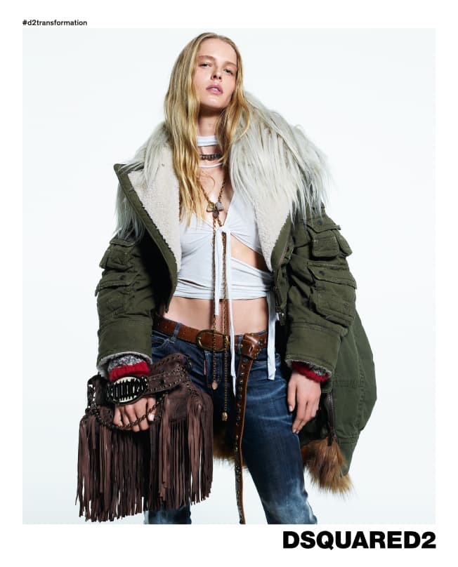 Model in green parka with faux fur collar wearing a white top and jeans holding a fringed brown handbag against white background