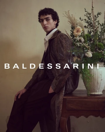 A seated male model wearing a patterned coat next to a floral arrangement for the Baldessarini Fall 2024 campaign.