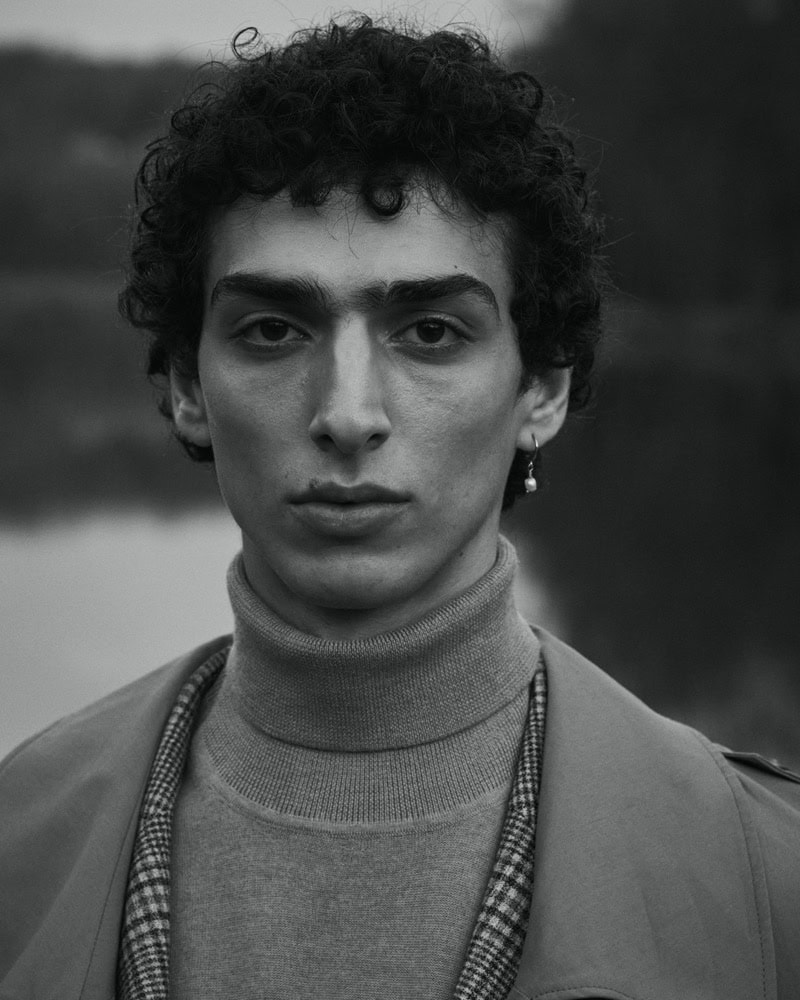 Portrait of a man with curly dark hair wearing a turtleneck and coat, photographed by Andreas Ortner for Baldessarini.