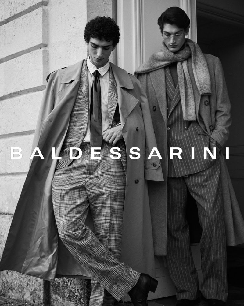 Two men in tailored suits and coats posing outdoors against an architectural stone wall for Baldessarini fall campaign