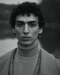 Portrait of a man with curly dark hair wearing a turtleneck and coat, photographed by Andreas Ortner for Baldessarini.