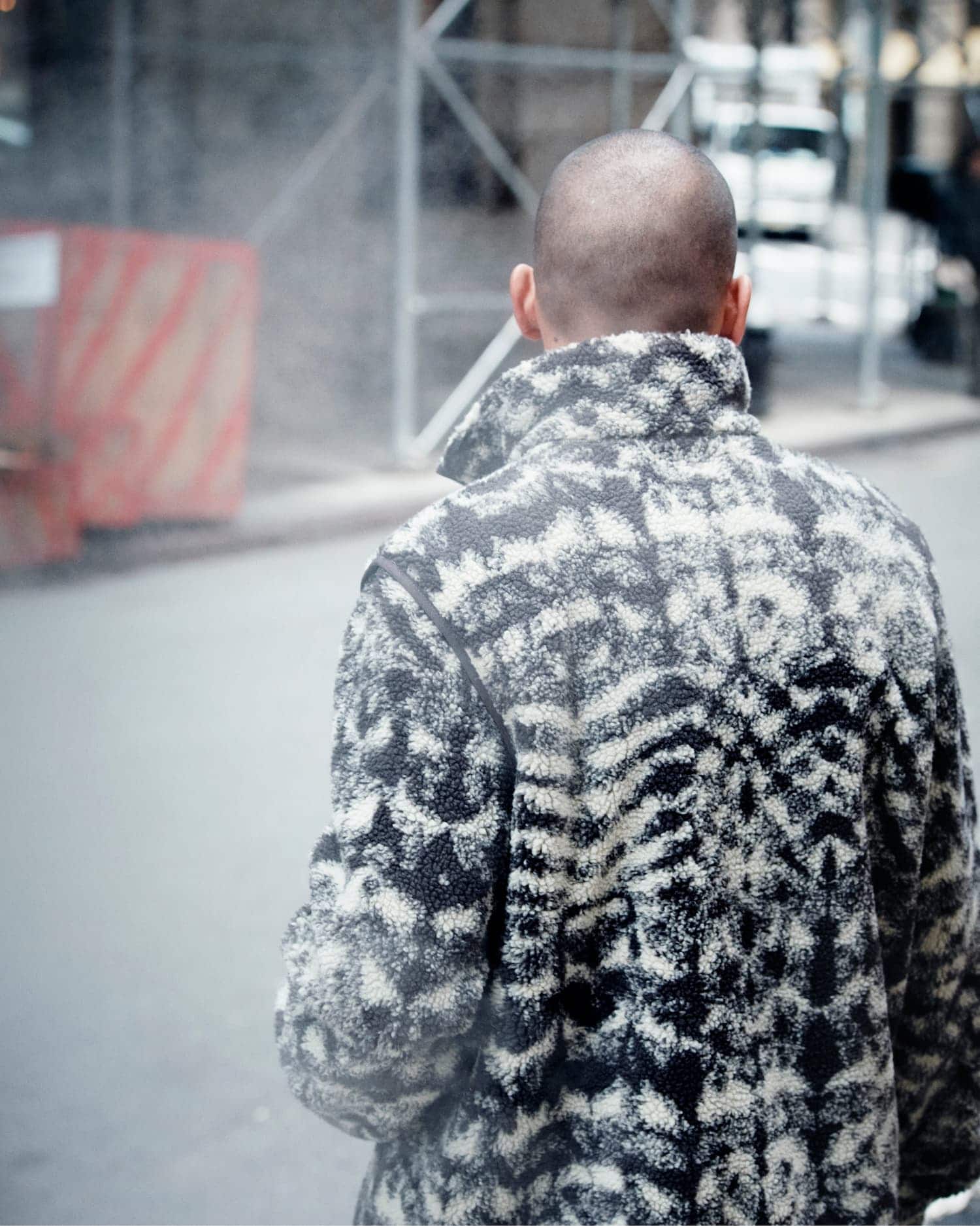 Man from behind wearing a patterned fleece jacket walking on a city street