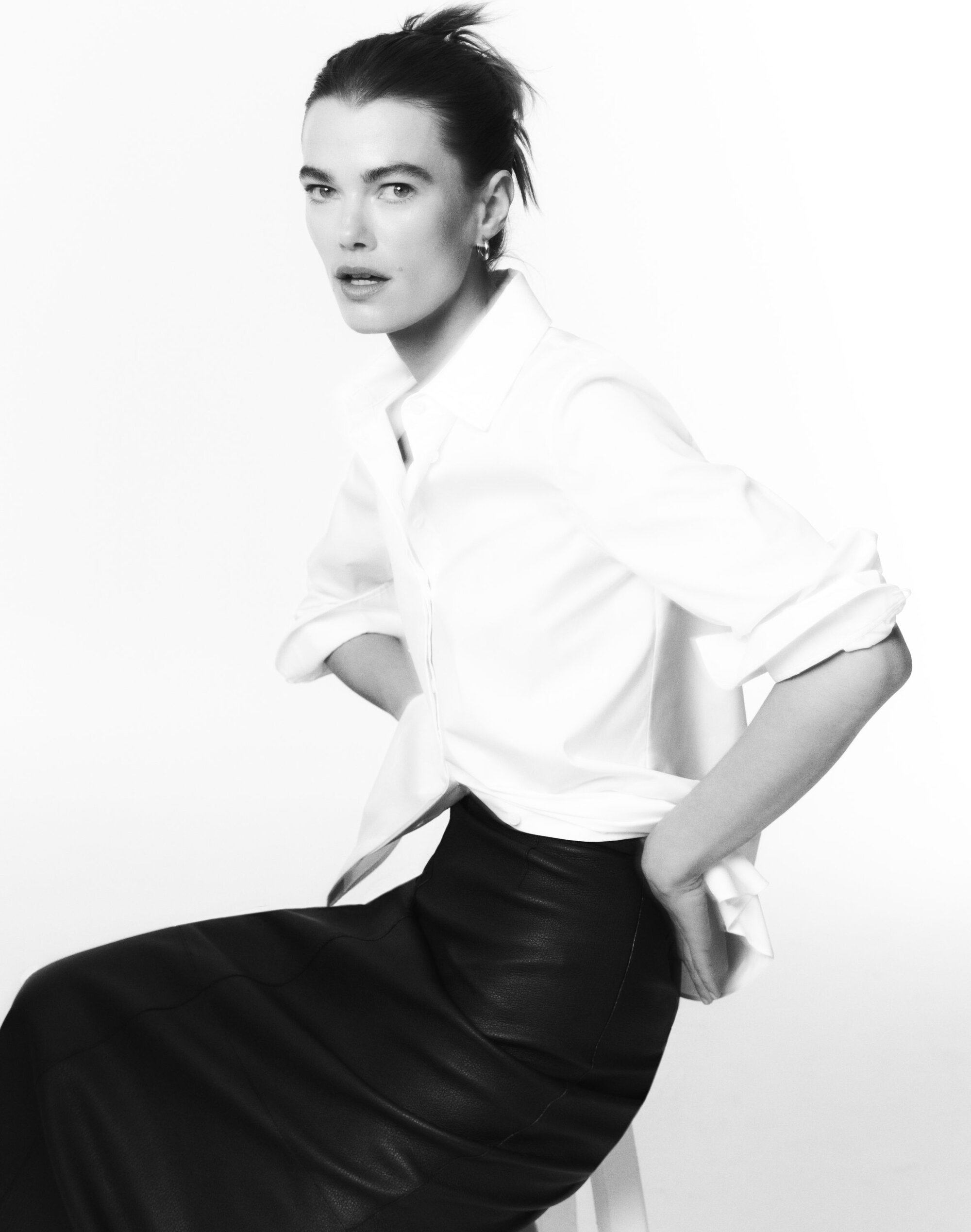 Model wearing white button-down shirt and black skirt against a plain white studio background