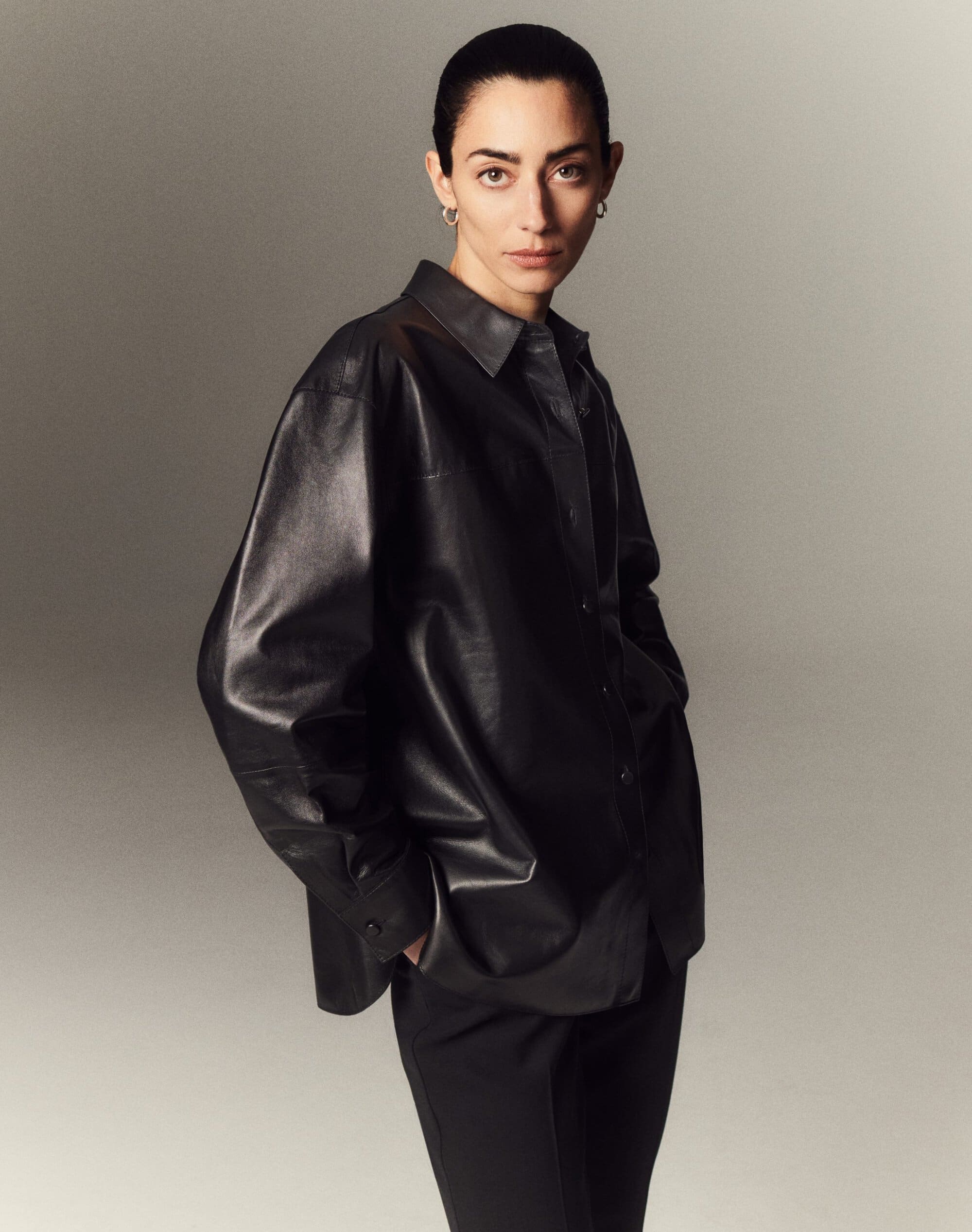 Model wearing a black leather shirt standing against a neutral studio background