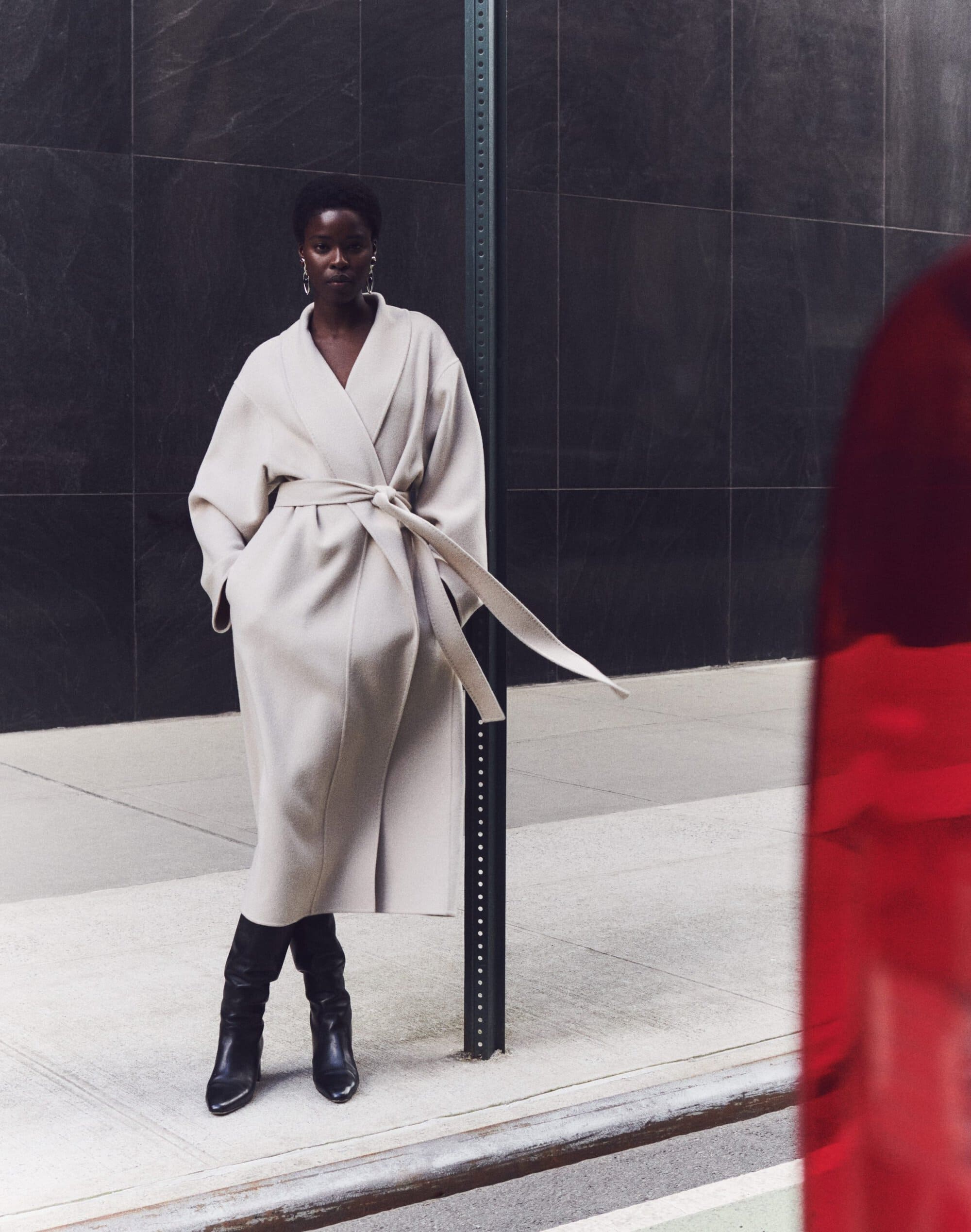 Model in a cream wrap coat and black boots standing against a dark tiled wall for Lafayette 148 Fall 2024 campaign