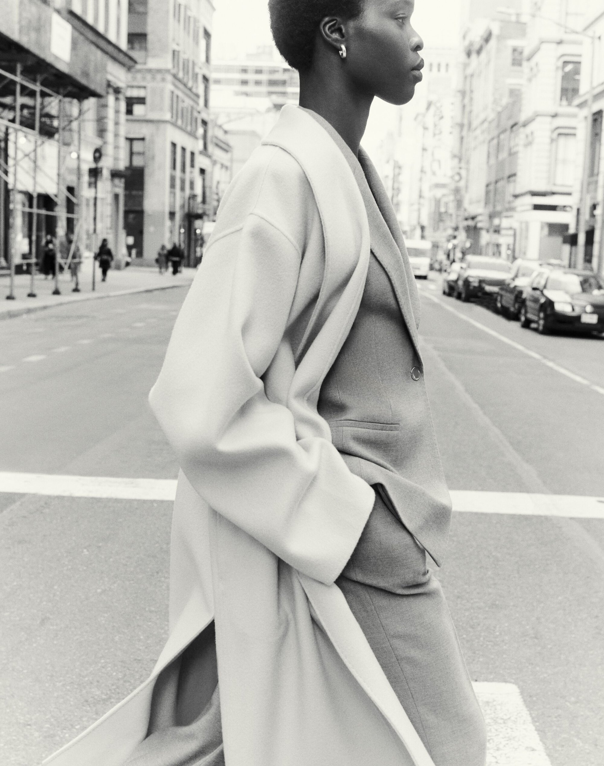 Model wearing a long coat walking on a city street in a black and white fashion campaign image