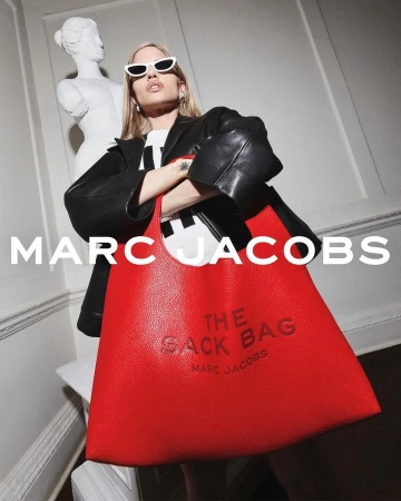 Model in white sunglasses and black leather jacket holding a large red shoulder bag for Marc Jacobs