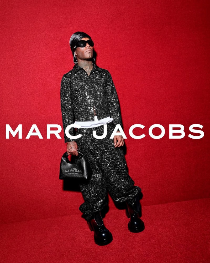 Lil Uzi Vert wearing a glittering dark suit and holding a black handbag against a red background for Marc Jacobs Fall 2024 campaign