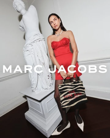 Model Irina Shayk wearing a red dress and zebra print tote bag beside a classical white marble statue for Marc Jacobs