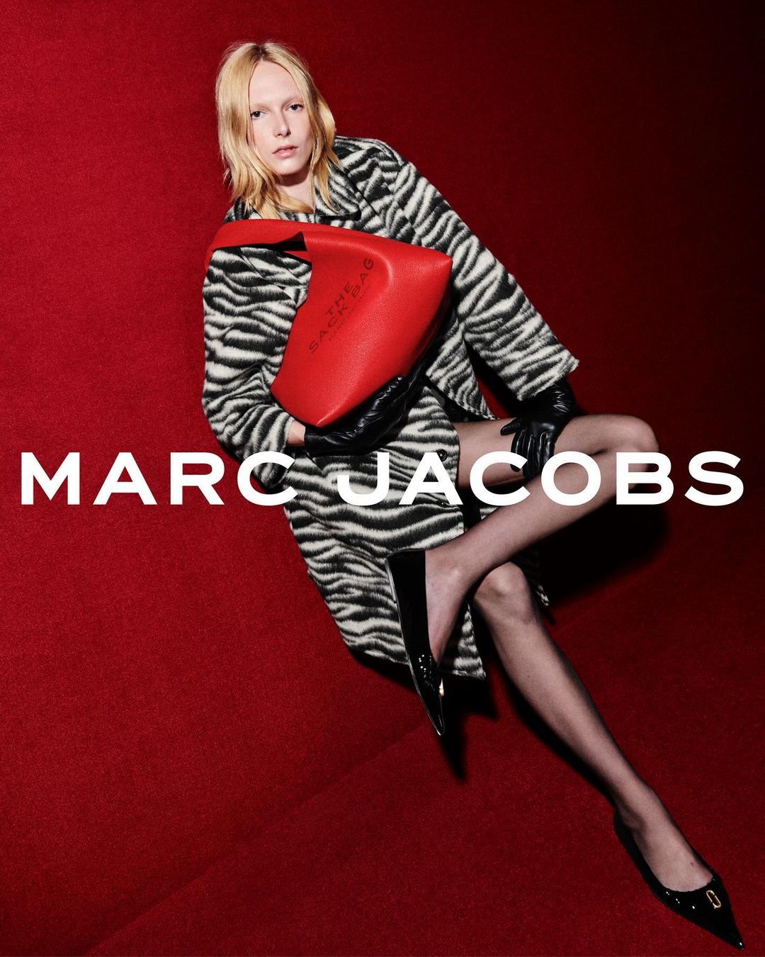 Model in zebra print coat holding red leather handbag against deep red background