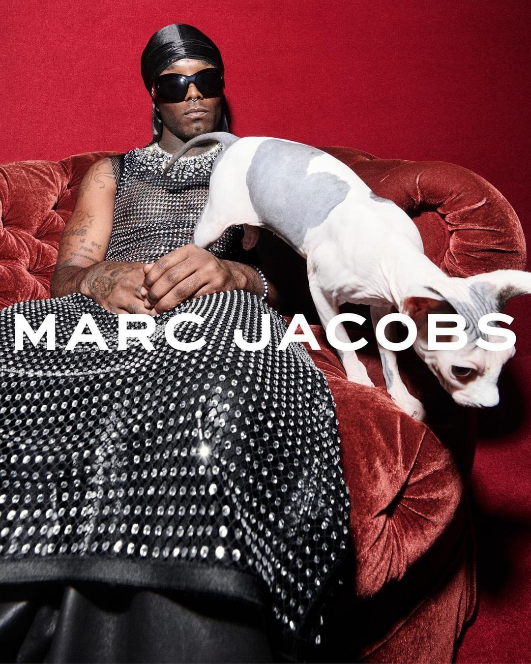 Lil Uzi Vert wearing embellished mesh dress and sunglasses seated on red velvet couch with a hairless cat for Marc Jacobs Fall 2024 campaign.
