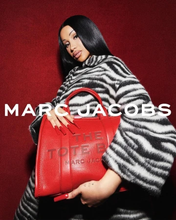Cardi B holding a red tote bag wearing a black and white zebra print coat against a textured red background