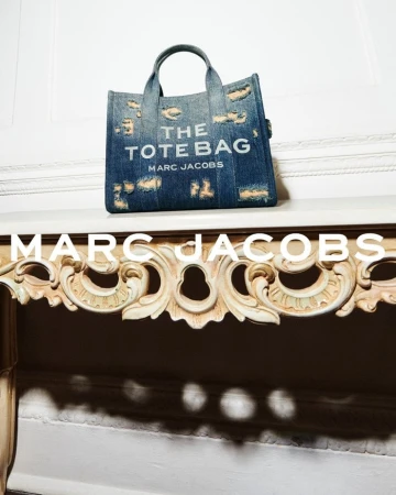 Distressed denim tote bag resting on an ornate carved console table against a white wall.