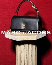 Black leather handbag with gold hardware displayed on an antique carved pedestal against a red textured background