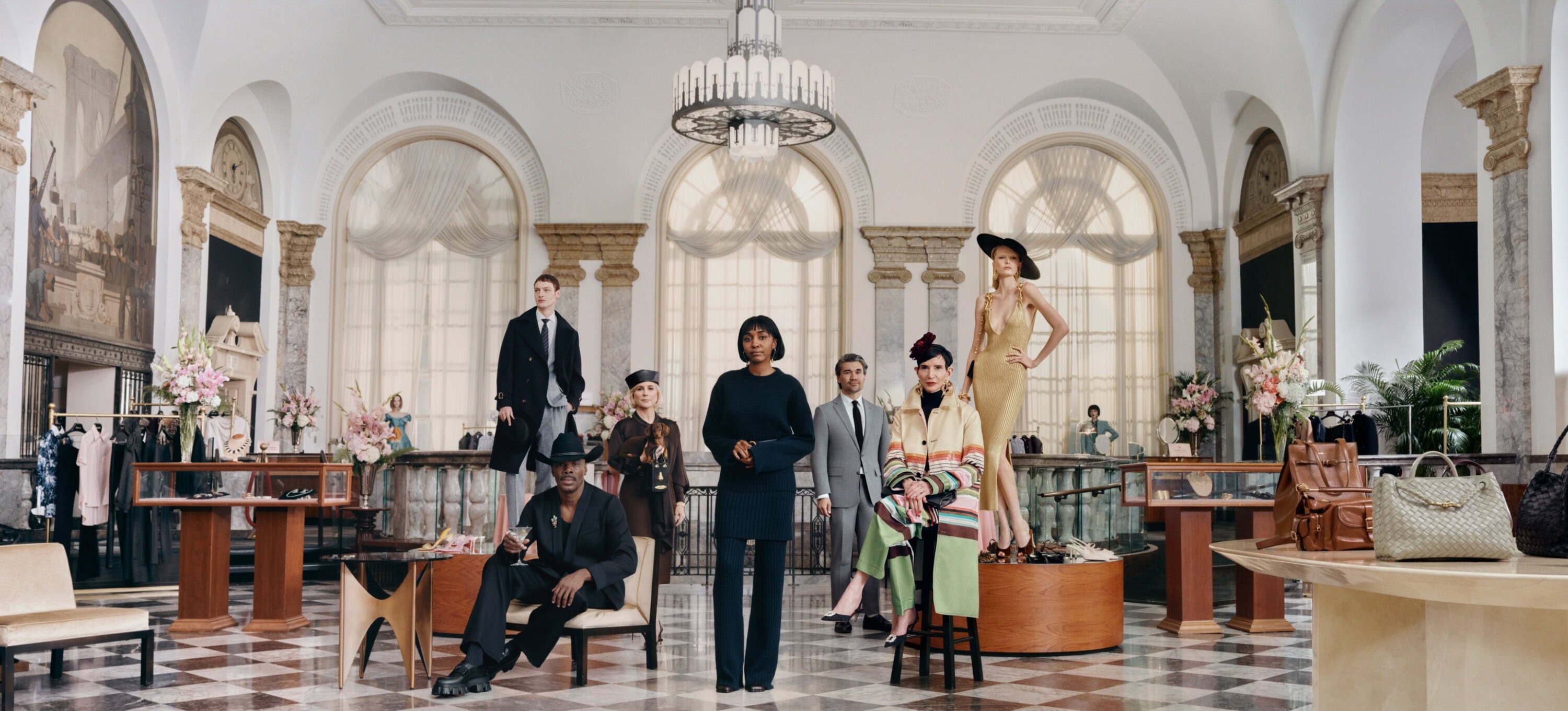 Group of models in luxury fashion posing inside a grand hotel lobby with checkerboard floors and tall arched windows.
