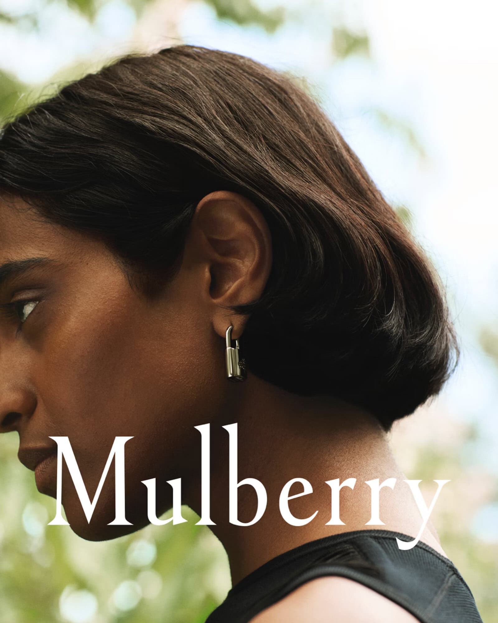 Profile portrait of a woman wearing a padlock earring and dark top for the Mulberry Fall 2024 campaign, photographed by Guen Fiore.