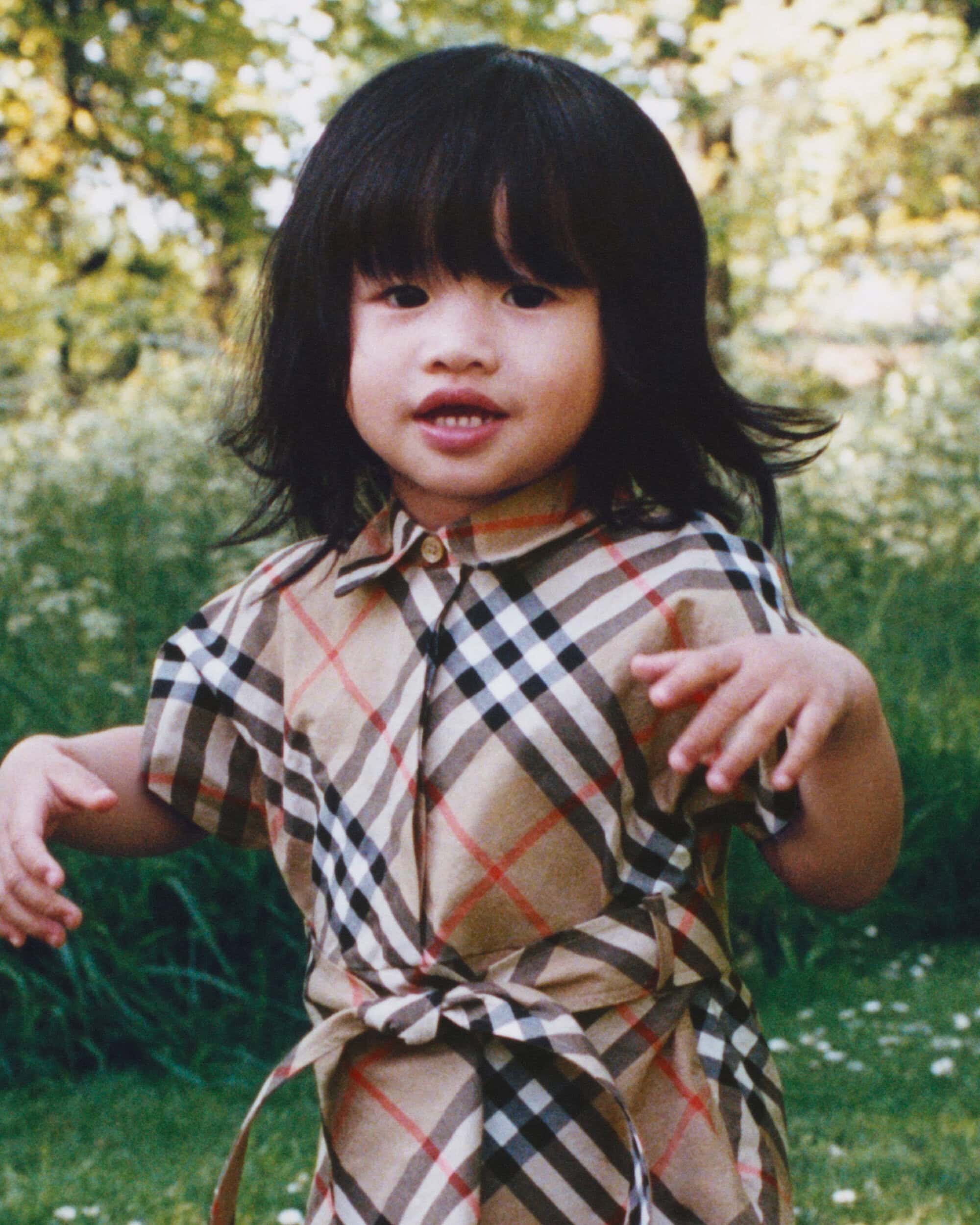 Young child in a Burberry plaid dress standing outdoors in a garden setting