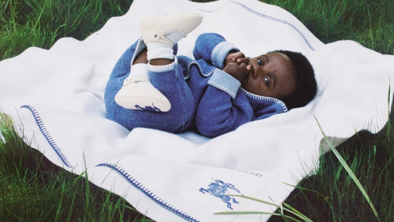 Baby wearing blue knit outfit and white booties lying on a white blanket spread over green grass