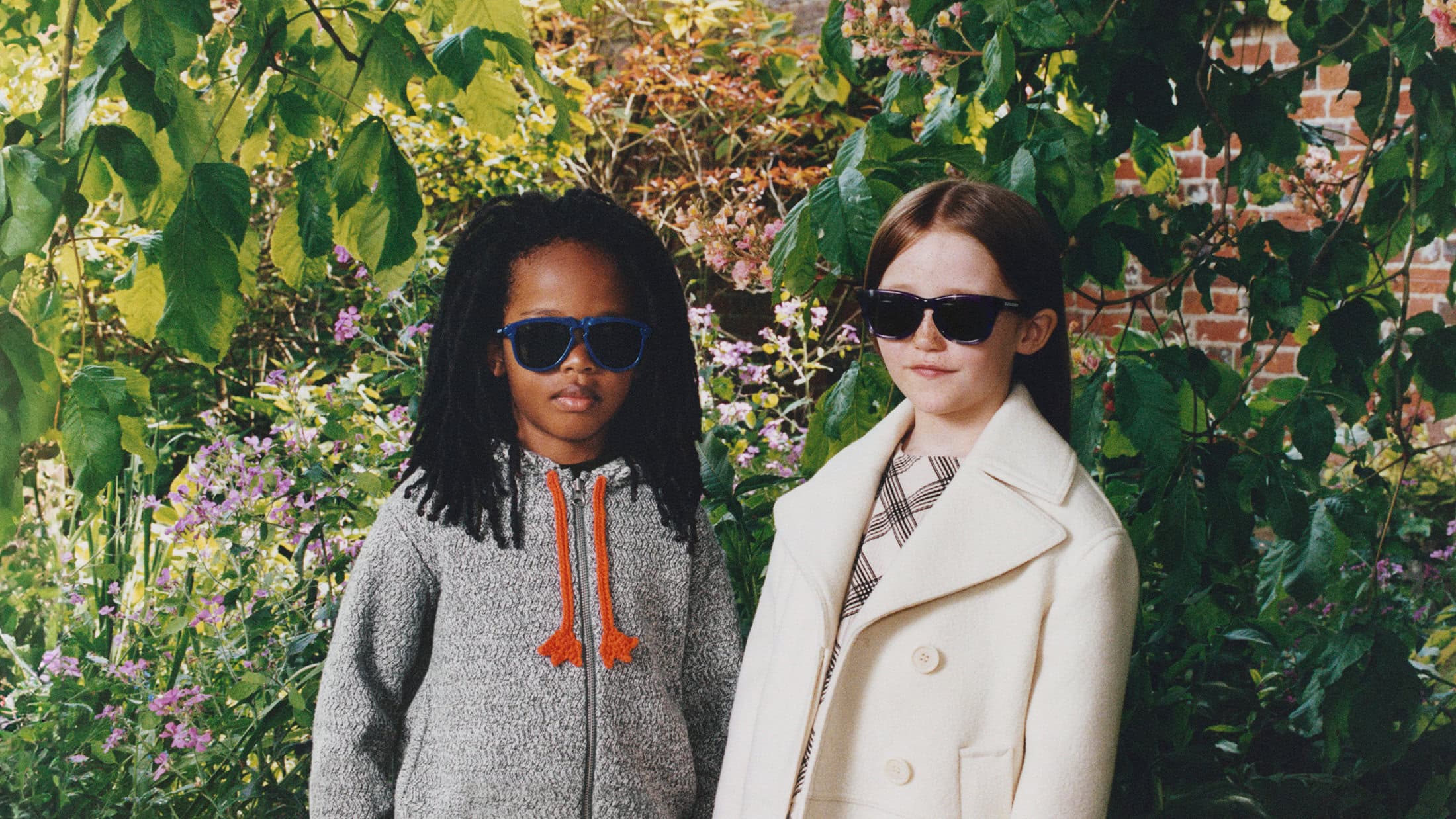 Two children wearing sunglasses outdoors in a garden setting, photographed by Rosie Marks for Burberry.