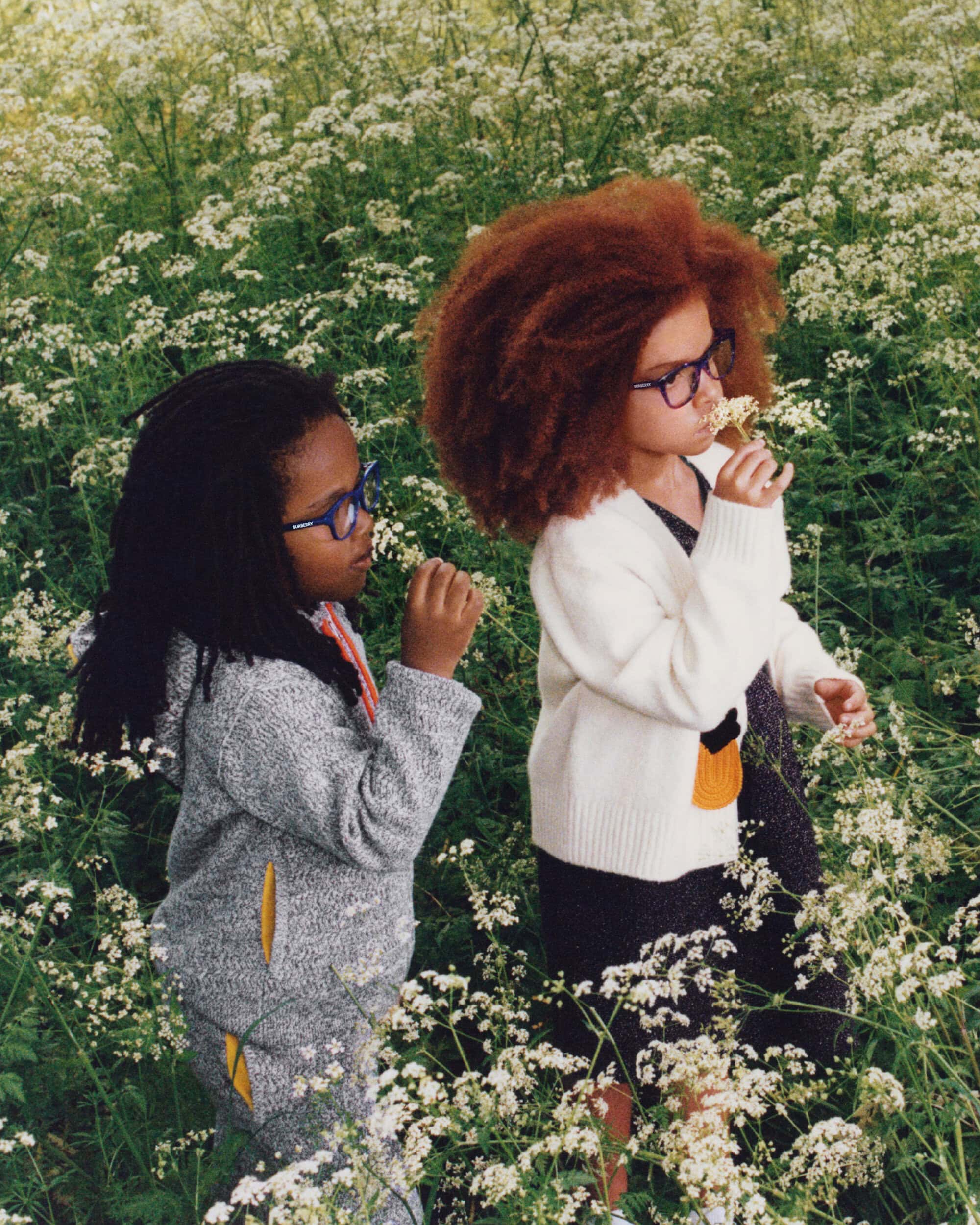 Two children wearing glasses and knitwear standing among white wildflowers in a field for Burberry.