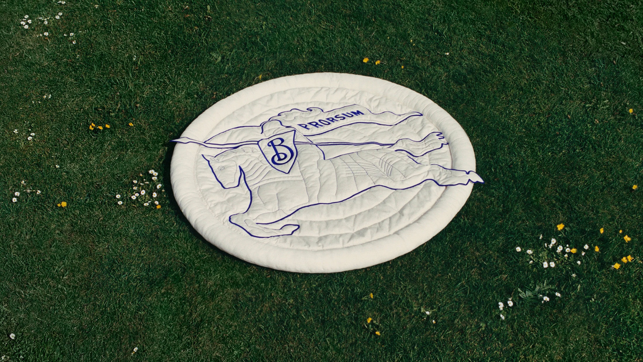 Round white quilted mat with embroidered blue Prorsum equestrian knight logo laid on green grass