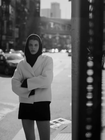 Model in a cream jacket and dark hooded sweater standing on a city street for Soft Goat fall campaign.